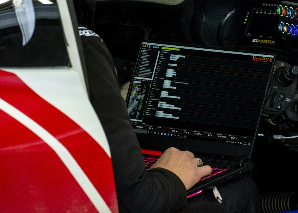 Hands on a laptop running ECU tuning software inside a race car