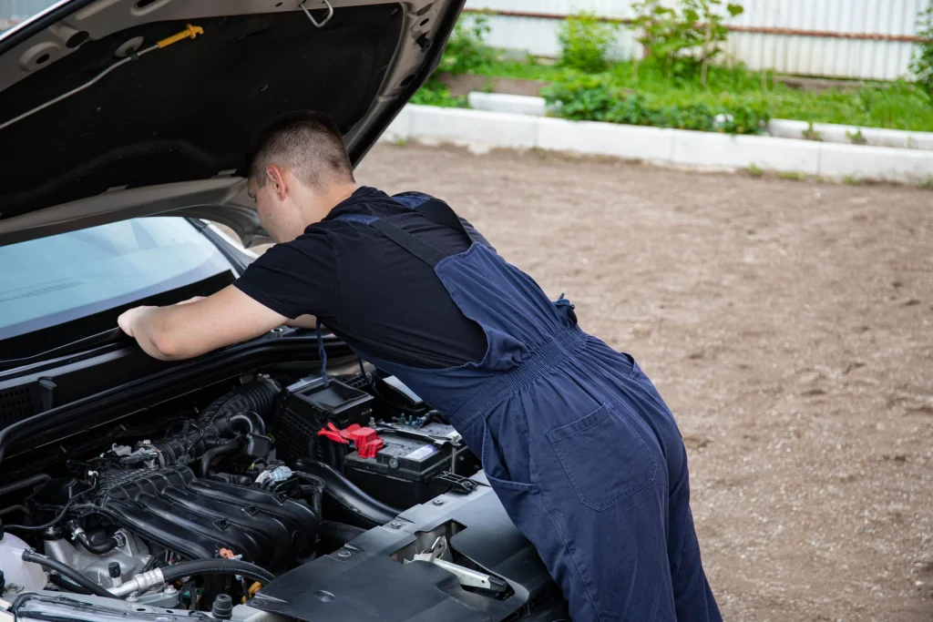 Mechanic in blue overalls leaning into an open engine bay outdoors
